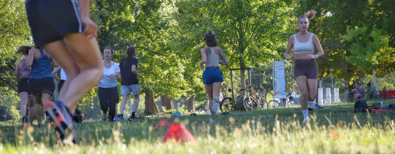 Fitness-Kurs in der Friedrichsau. Menschen joggen auf der Wiese im Sommer.